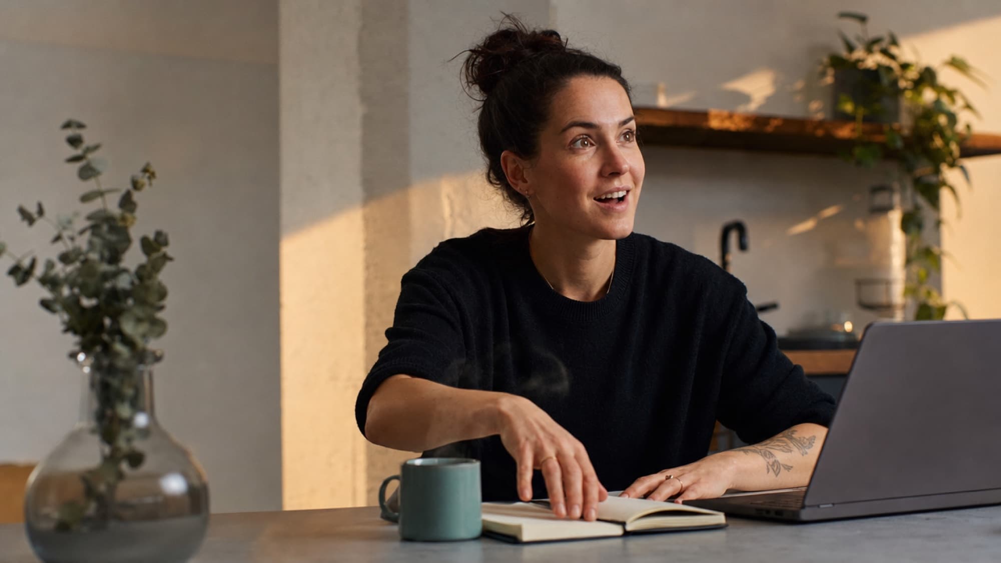 A woman at her kitchen table at dawn, lighting up mid-conversation with her laptop